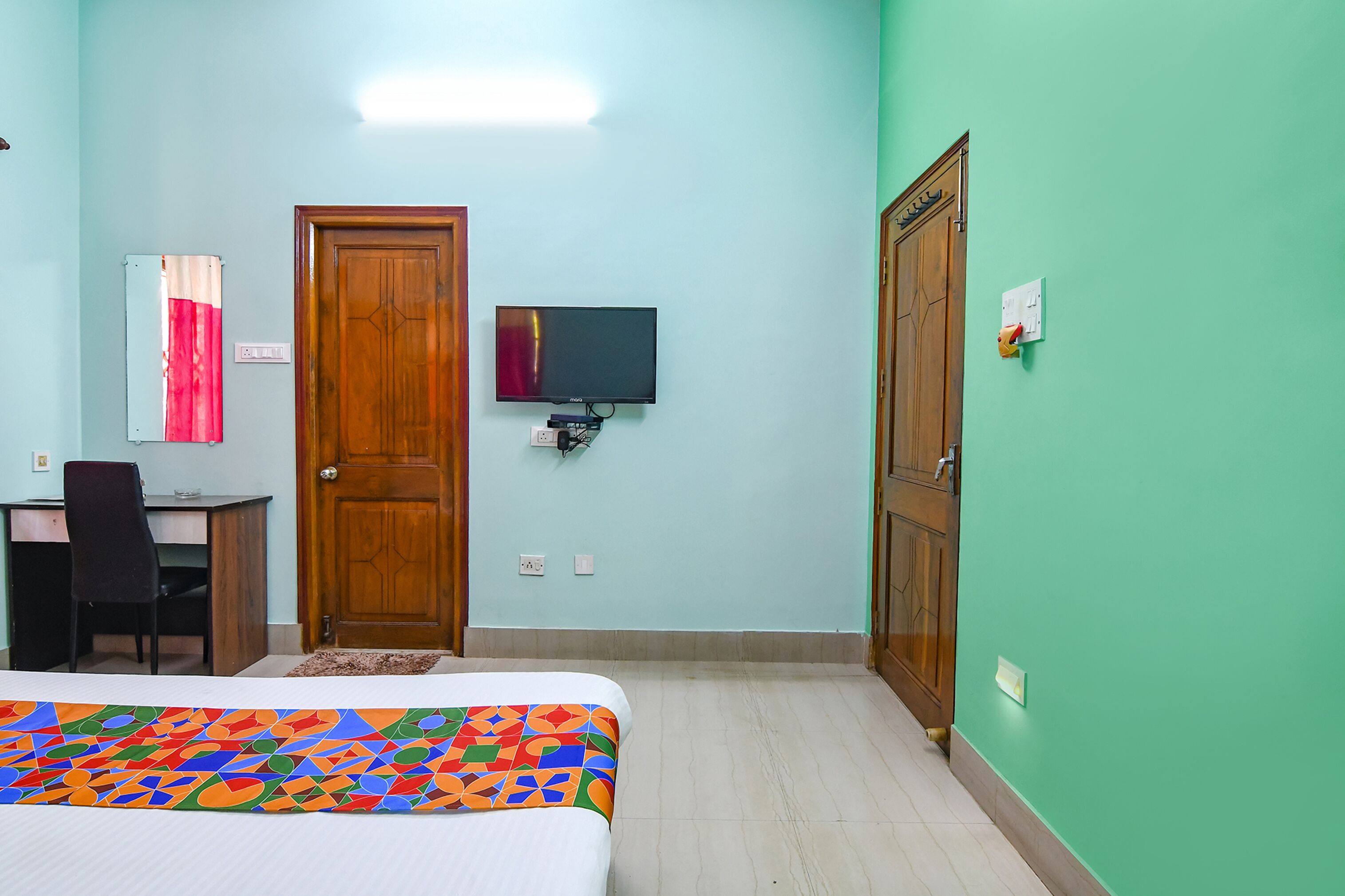 A room with a bed, a desk, a chair, a television, and two doors.