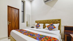 Una cama bien hecha con un edredón geométrico de colores, un cabecero de madera y una mesita de noche con una lámpara.