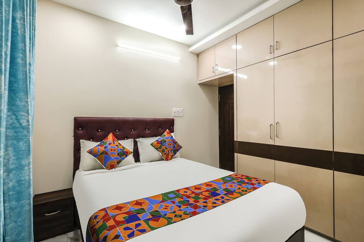 Quarto de hotel com uma cama, mesa de cabeceira, guarda-roupa e ventoinha no teto.