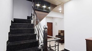 Un escalier avec des marches noires et des rampes en métal, menant à une pièce où se trouvent un bureau en bois et un téléviseur fixé au mur.