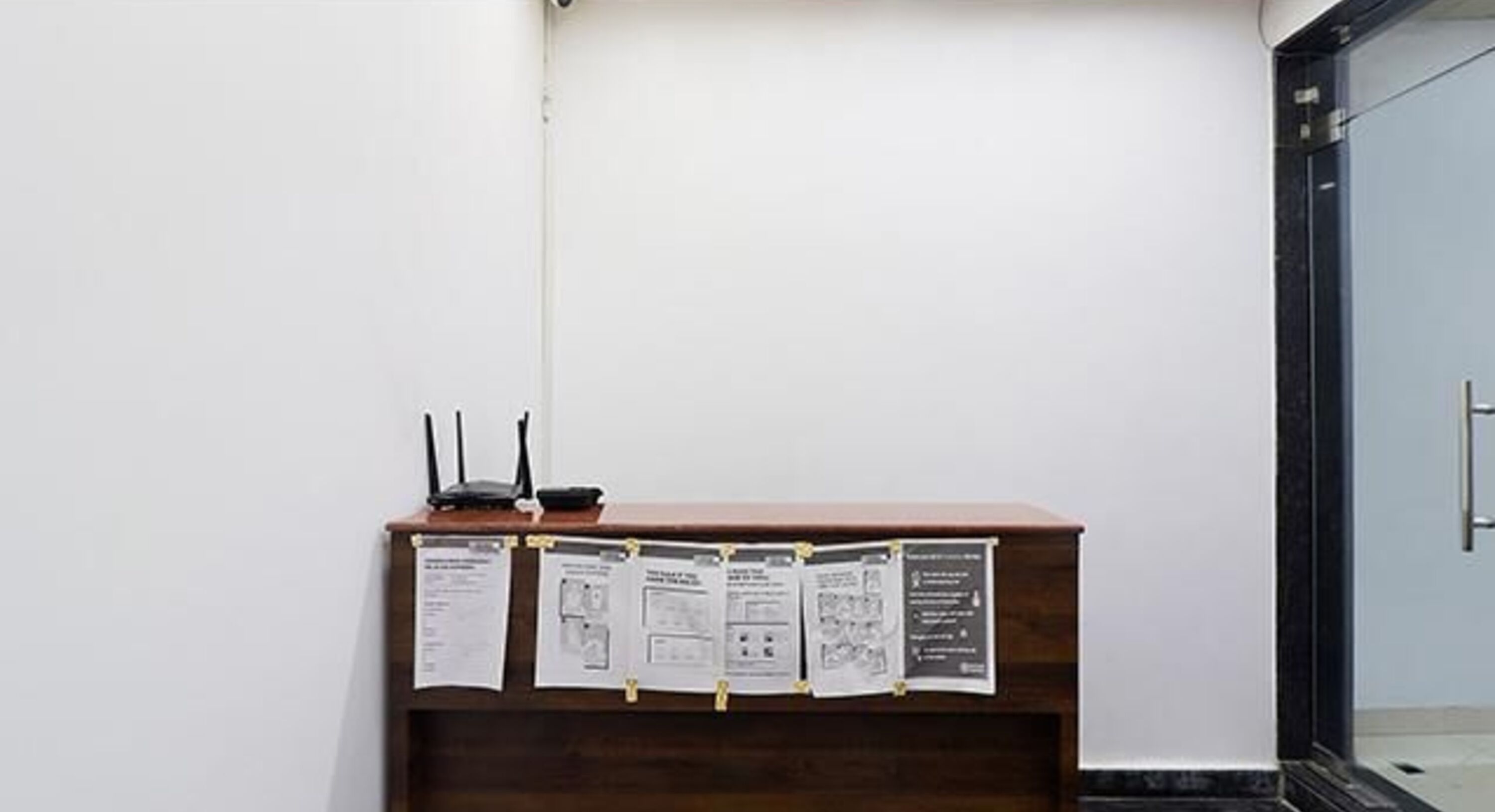 A reception desk with a wooden finish, a black router, and several informational posters attached to the wall.