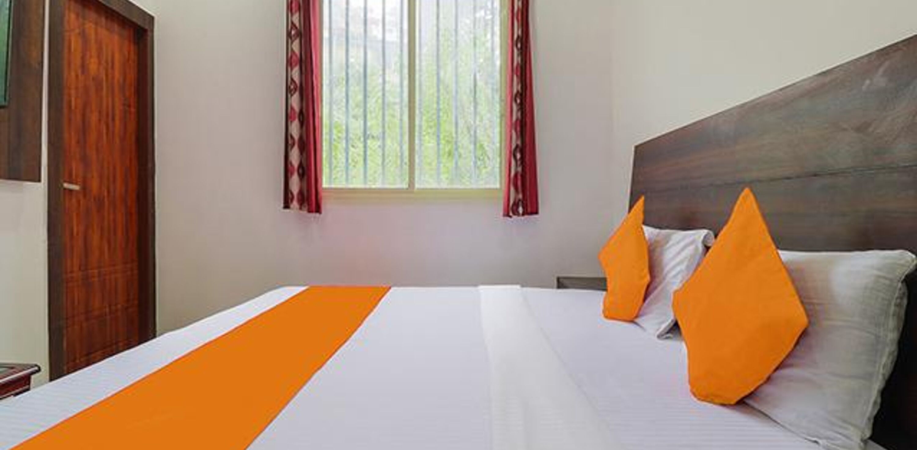 A hotel room with a bed, a window with curtains, and a wooden headboard.