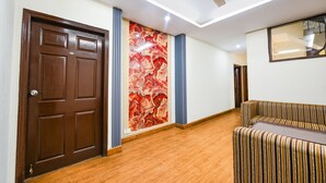 A hallway with a wooden floor, a brown door, a ceiling fan, and a striped sofa. - Fabhotel Mosca (Gurugram)
