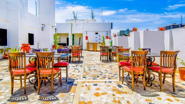 Eine Terrasse im Freien mit Holztischen und -stühlen, einem gefliesten Boden und weißen Wänden.
