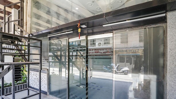 A modern building entrance with glass doors, a metal staircase, and a reflection of a street scene. - Fabexpress Arjun Imperial (Raipur)