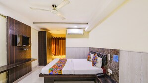 A hotel room with a bed, a TV, a ceiling fan, an air conditioning unit, a bedside table, and a nightstand. - Fabexpress Arjun Imperial (Raipur)