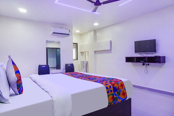 Una habitación de hotel con cama, televisión, aire acondicionado y ventilador de techo.