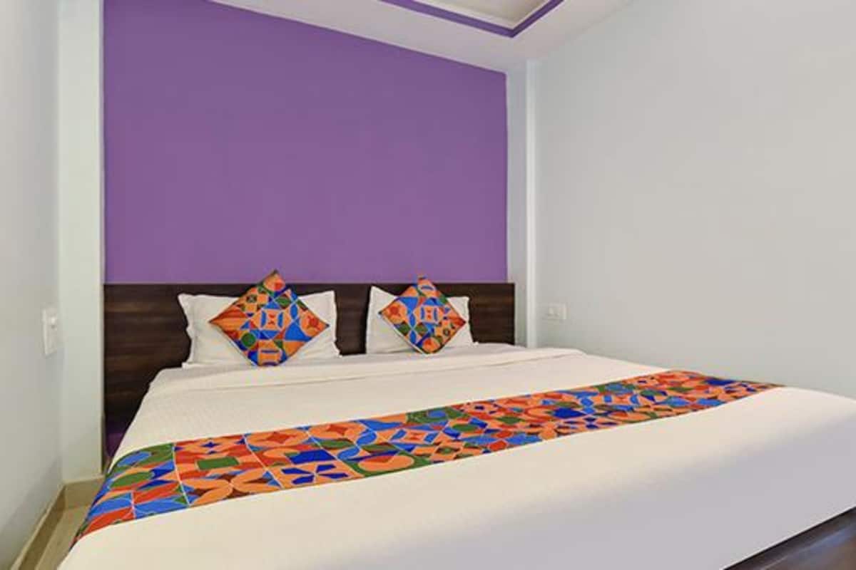A hotel room with a bed, a purple accent wall, and a colorful bedspread.