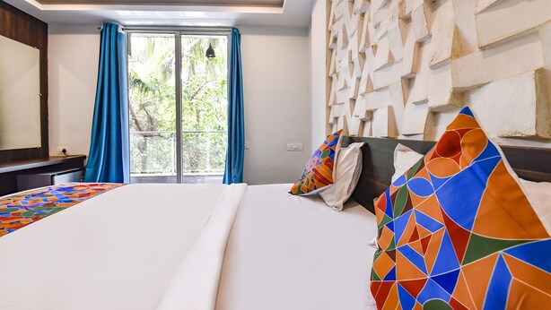 A hotel room with a large bed, a view of greenery through the window, and a unique textured wall. - FabHotel Arambol Inn (Arambol)
