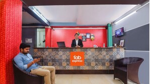 A reception area with a red wall, a 'fab express' sign, a laptop, and a person sitting on a chair. - FabHotel Arambol Inn (Arambol)