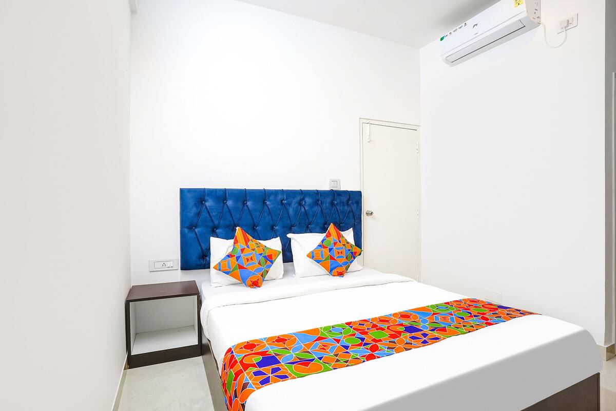 Une chambre à coucher avec une tête de lit bleue à motifs capitonnés, du linge de lit blanc et une couvre-lit aux motifs géométriques colorés.