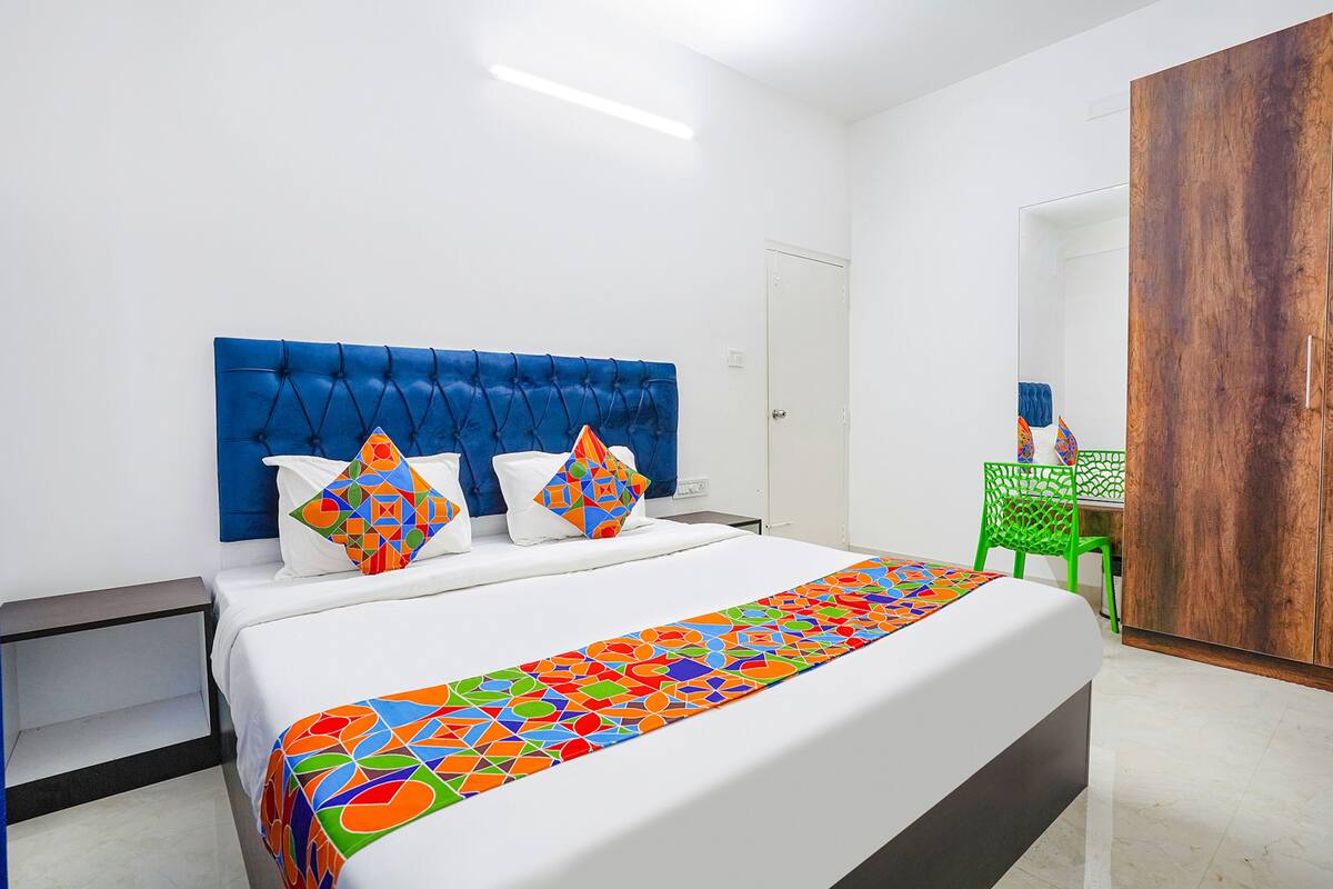 Un lit avec une tête de lit bleue, une literie blanche et un couvre-lit aux motifs géométriques colorés.