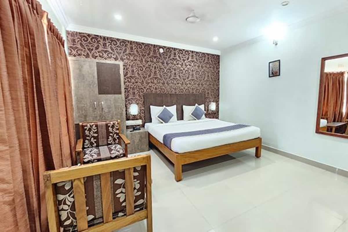 A bedroom with a bed, bedside tables, a chair, a mirror, and a patterned wall.