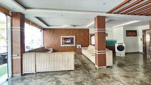 A spacious lobby with a sectional sofa, a television mounted on a wooden wall, and a washing machine in the background. - Fabhotel Prime Ministers Kourt (Somvarpet)