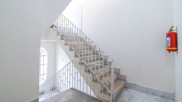 A staircase with a metal railing, a fire extinguisher mounted on the wall, and a window with a view of another room. - Fabexpress Vedika (Kolkata)