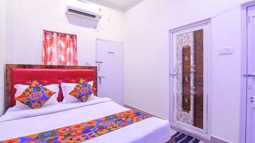 A hotel room with a bed, an air conditioner, a door, and a window with curtains.