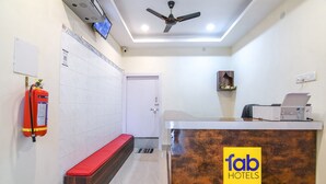 A hotel reception area with a reception desk, a ceiling fan, a fire extinguisher, a bench, and a door. - Fabexpress Vedika (Kolkata)