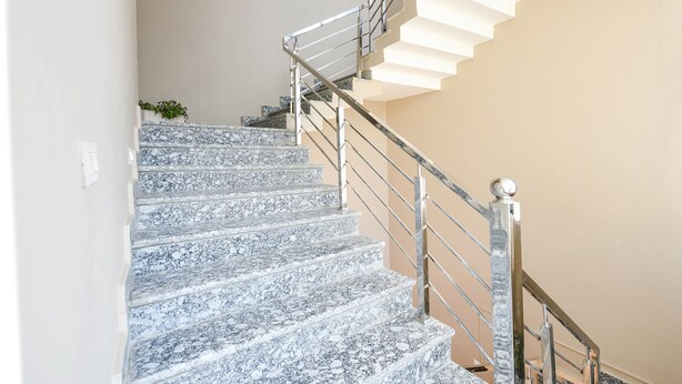 Una escalera con barandilla de metal y escalones de mármol.