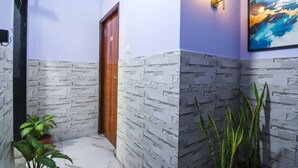 A hallway with a patterned wall, a wooden door, a potted plant, and a wall-mounted light fixture. - FabHotel Srideep (Kolkata)