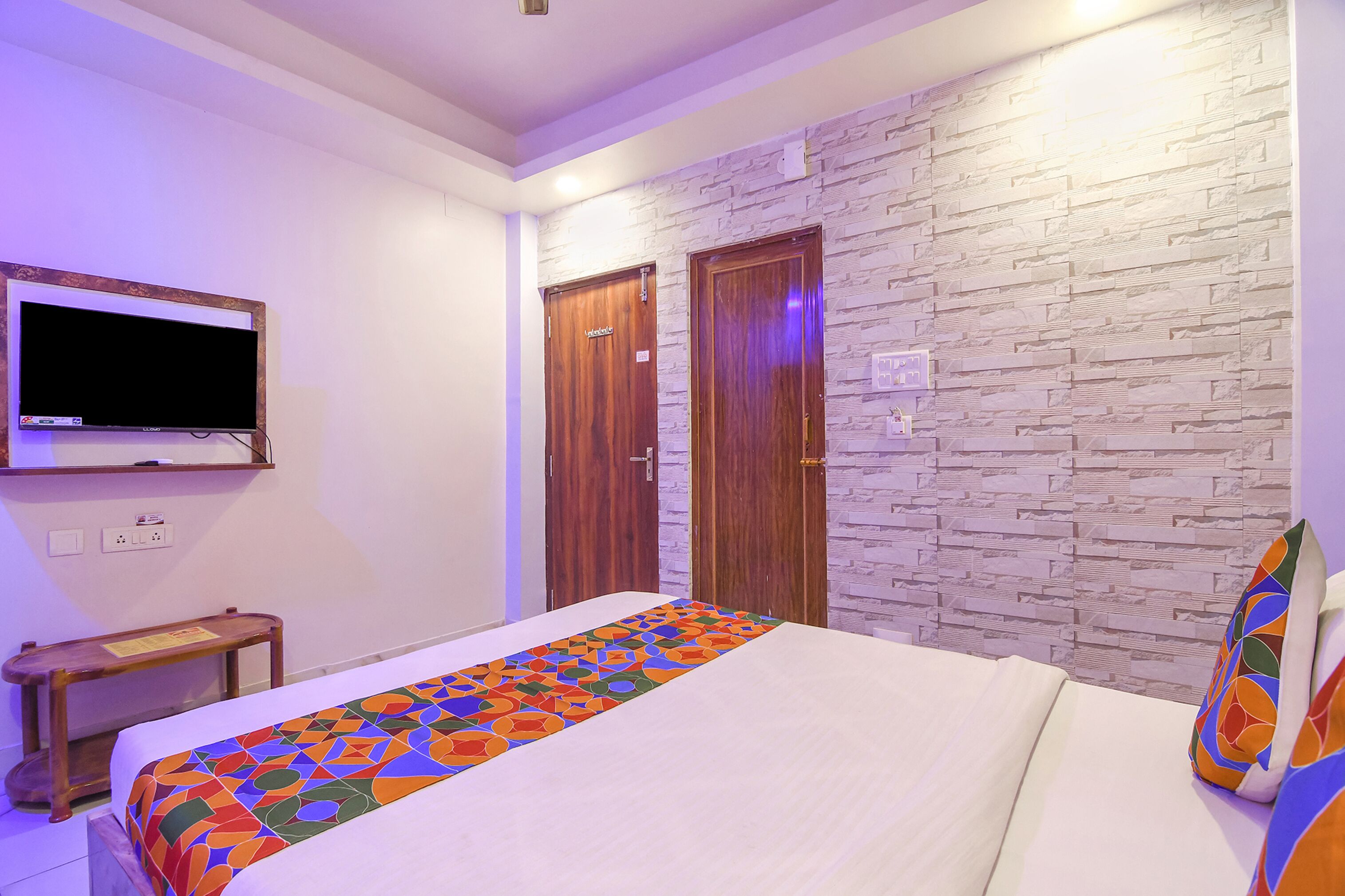 A hotel room with a bed, a TV mounted on the wall, and two wooden doors.