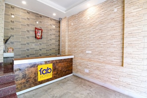 Zona de recepción de un hotel con diseño moderno, que incluye un mostrador de recepción con un logo y una pared decorada con un motivo.