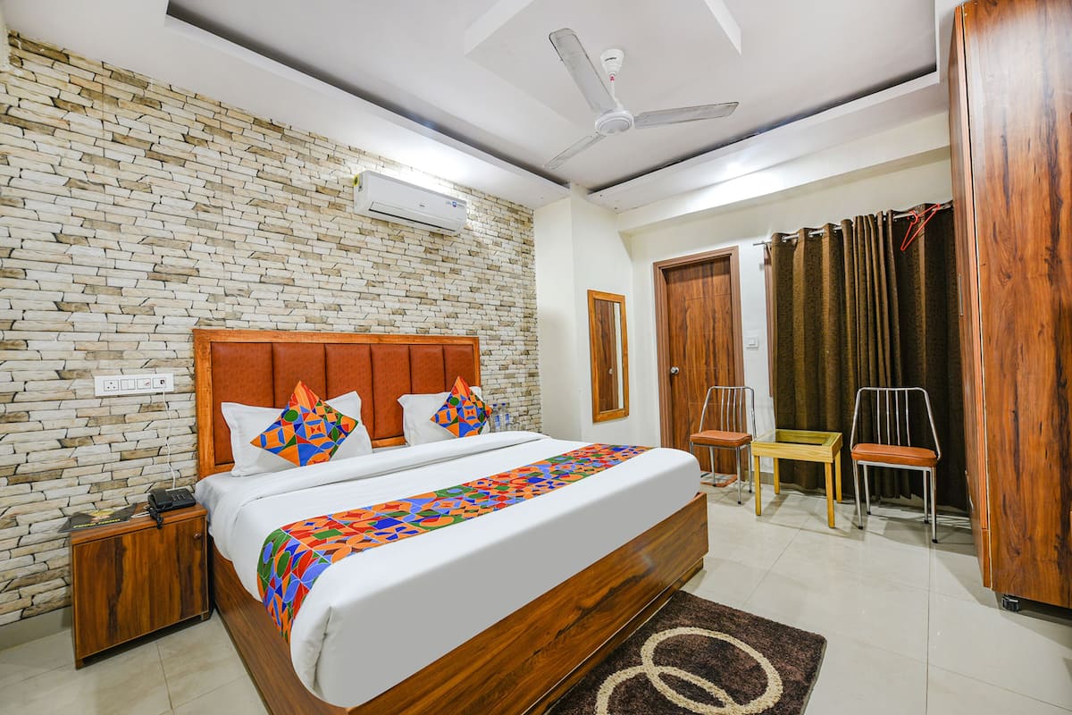 A hotel room with a brick-patterned wall, a wooden bed, a ceiling fan, and a view of the outside through a window with curtains.
