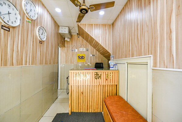 Zona de recepción de un hotel con un mostrador de madera, un banco y varios relojes en la pared.