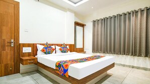 A modern hotel room with a large bed, wooden headboard, and a view of the city through curtains.