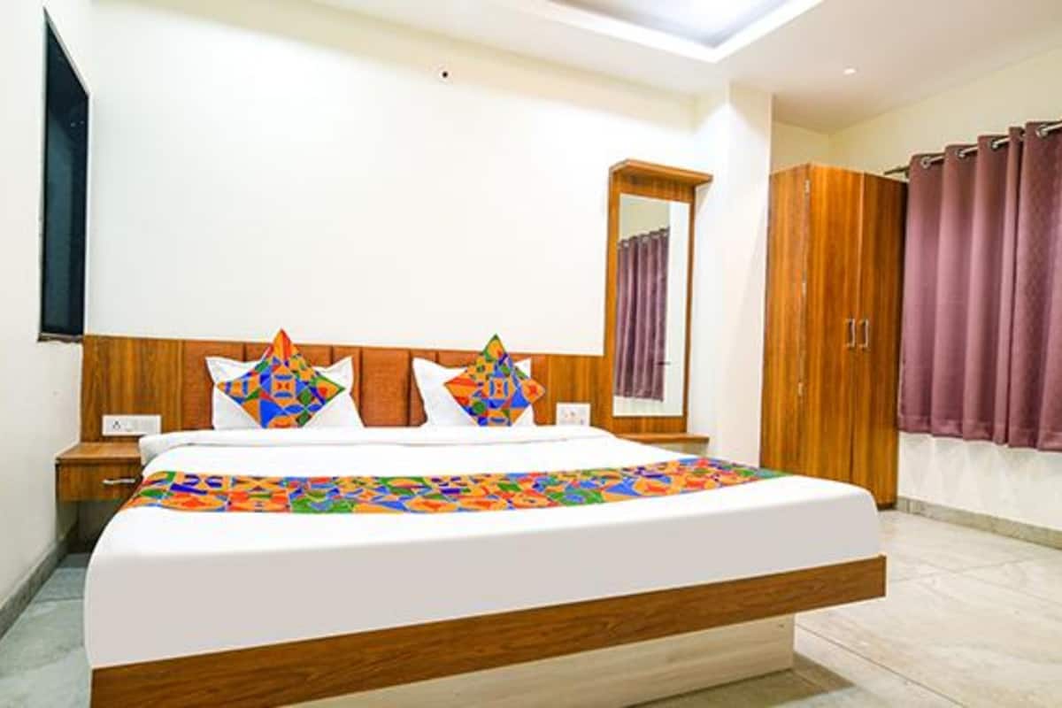 A neatly arranged hotel room with a large bed, wooden headboard, a mirror, a wardrobe, and a window with curtains.