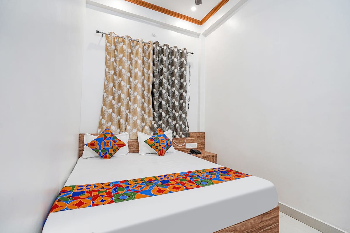 Una cama bien tendida con una colcha geométrica colorida, dos almohadas y una mesita de noche de madera con un teléfono.