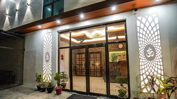 Entrada de hotel con puerta de vidrio, plantas en macetas y una pared decorativa con el símbolo 'Om'.