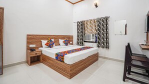 Un dormitorio con cabecera de madera, cama con manta colorida, mesita de noche con teléfono, ventana con cortinas estampadas y escritorio con silla.