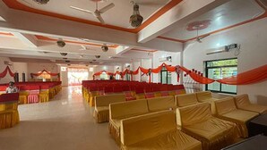 A spacious hall with rows of yellow chairs and red drapes, a ceiling fan, and a large window. - Fabhotel Kalawati Palace (Faizabad)