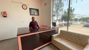 A reception desk with a dark wood finish and a red accent, a beige sofa, a clock, and a painting on the wall. - Fabhotel Kalawati Palace (Faizabad)