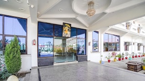 A spacious lobby with large windows, a chandelier, and potted plants. - FabExpress Savitri Resort (Sohawal)