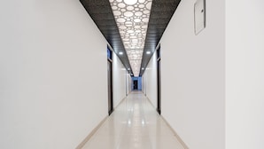 A long, narrow hallway with white walls and a shiny tiled floor. - FabExpress Savitri Resort (Sohawal)