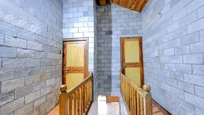 A narrow hallway with stone walls and wooden doors, leading to a room. - Fabhotel Attithi Huts And Cottage (Manali)