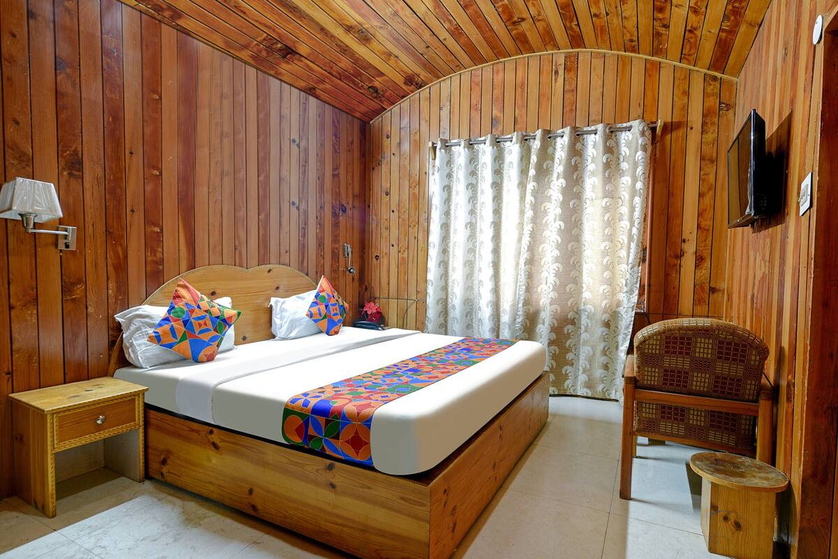 Ein Schlafzimmer mit Holzwänden, einem Bett, einem Nachttisch, einem Sessel und einem an der Wand befestigten Fernseher.