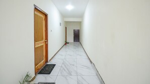 A hallway with a wooden door, a black mat at the entrance, and a tiled floor. - Fabhotel Paradise Guest House (Keylong)