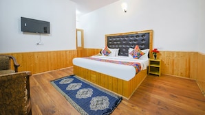 A bedroom with a wooden bed, a television mounted on the wall, and a small wooden nightstand with a vase of flowers. - Fabhotel Paradise Guest House (Keylong)