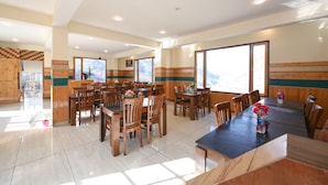A spacious dining area with multiple wooden tables and chairs, large windows offering a view of the mountains, and a wooden accent wall. - Fabhotel Paradise Guest House (Keylong)