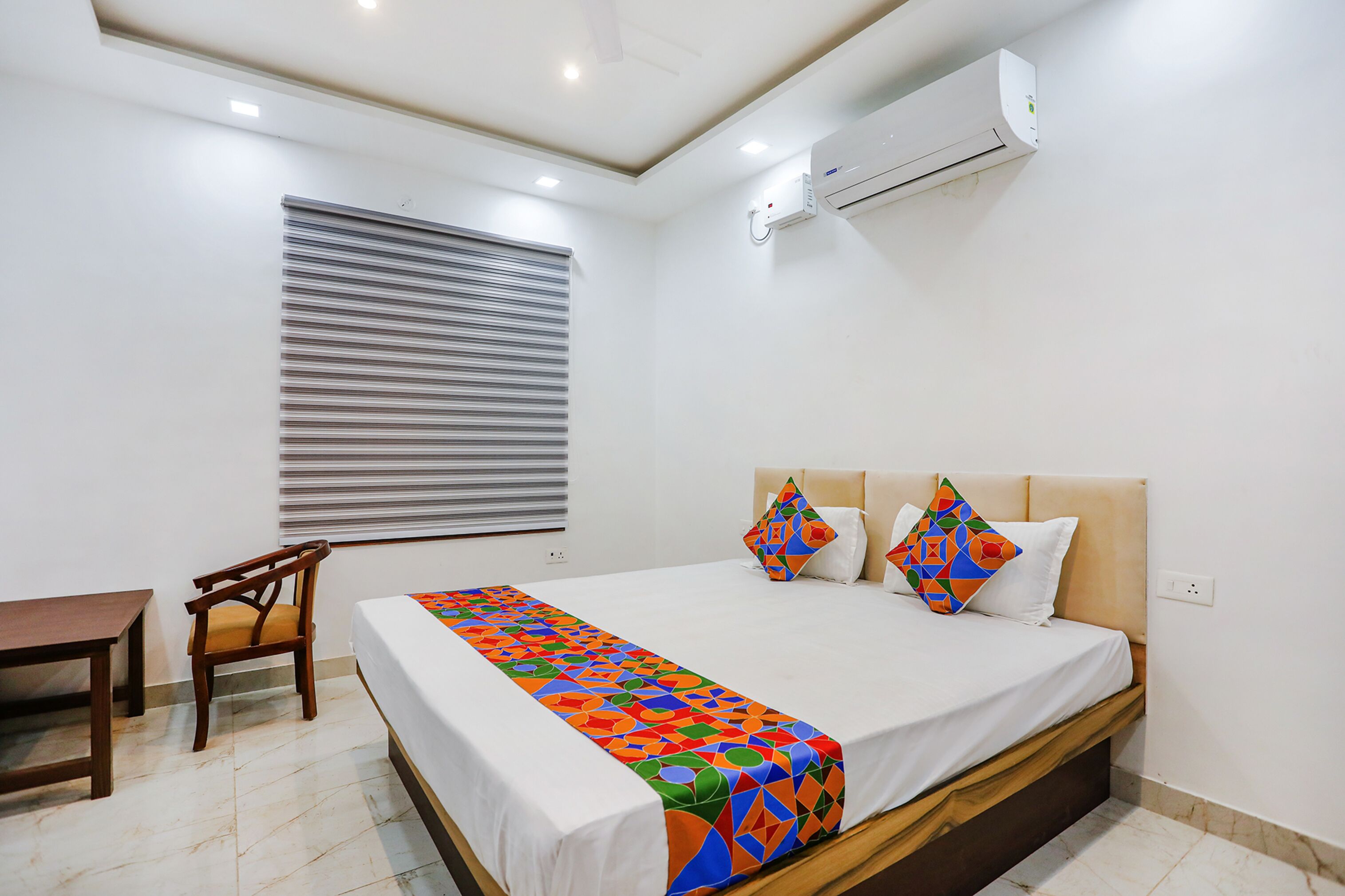 A hotel room with a bed, a chair, a desk, and an air conditioning unit.