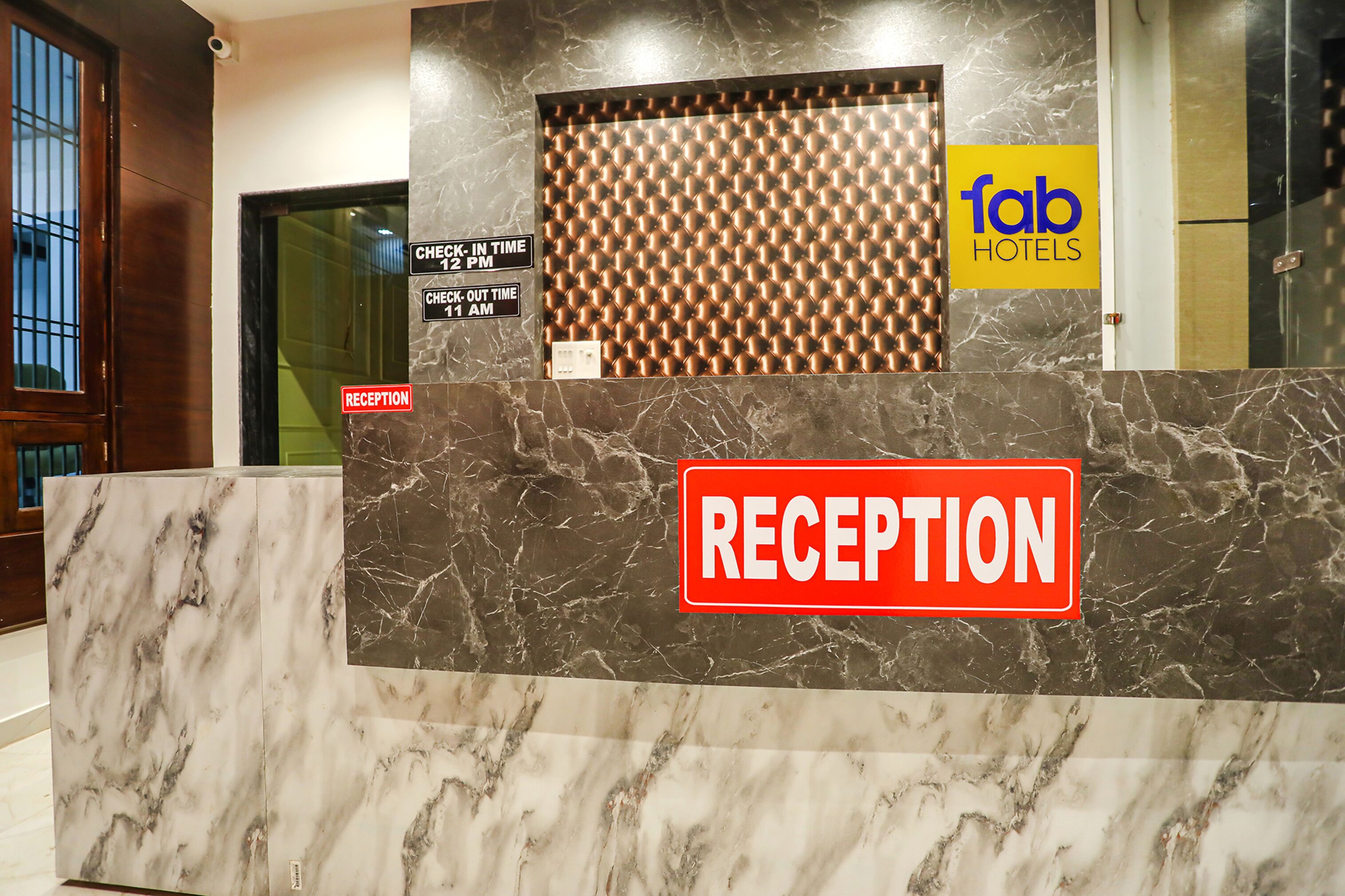 A reception desk with a marble counter, a sign indicating check-in and check-out times, and the logo of Fab Hotels.