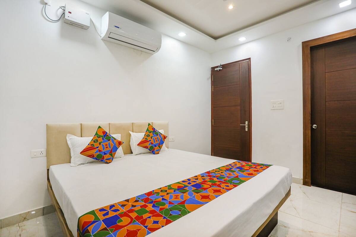 Habitación de hotel con cama, equipo de aire acondicionado, puerta de madera y pared blanca.