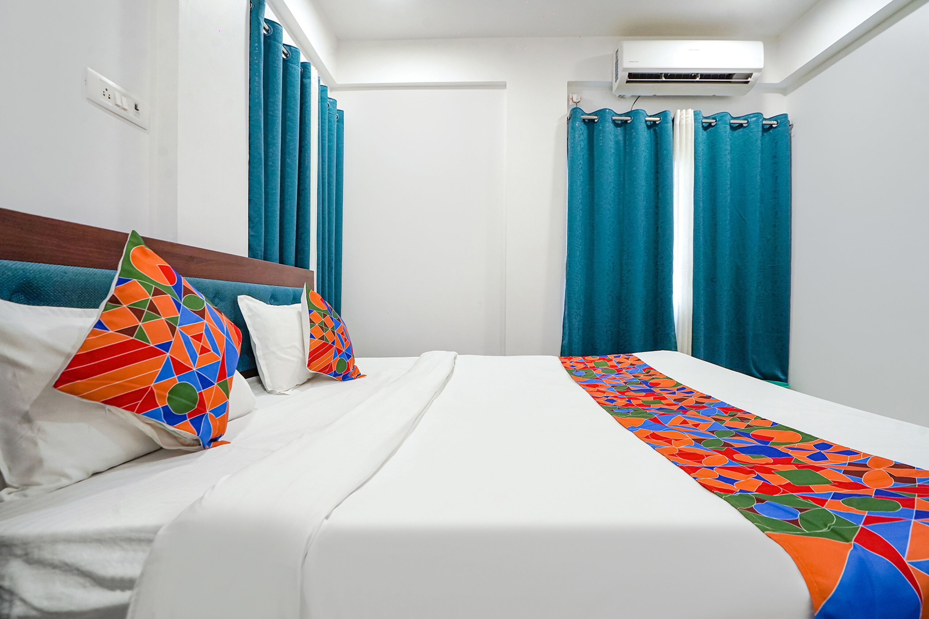 Une chambre d’hôtel avec un lit, un plaid aux couleurs vives et des rideaux turquoise.