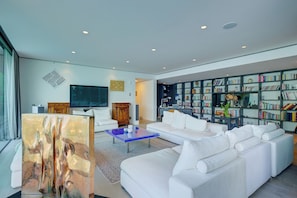A modern living room with a white sofa, a blue coffee table, a flat-screen TV, and a bookshelf filled with books.