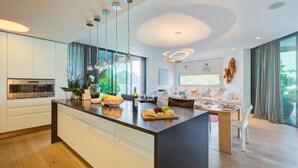 A modern kitchen with a central island, stainless steel appliances, and a dining area with a table and chairs. - Maison Sur l'Eau - Lugano Villa with View Terrace, Paradiso (Lugano), Switzerland (Paradiso (Lugano))