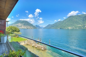 A balcony with a clear view of a lake, mountains, and a distant cityscape.