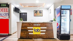 A reception desk at Fab Hotels with a wooden finish, a television above it, and a refrigerator to the right. - Fabhotel Royal City (Ahmedabad)