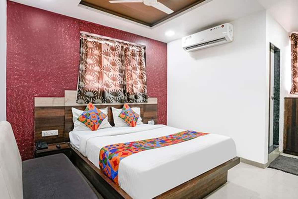 A bedroom with a bed, a nightstand, a desk, an air conditioner, and a window with curtains.